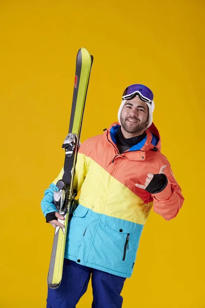 スノーボードの服を着た若い男がスキーをして手で黄色い背景のカメラを見て — ストック写真