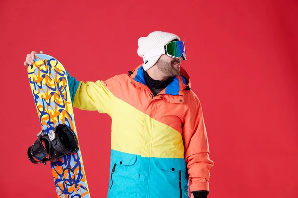 Glimlachende Man Sneeuwbril Houden Snowboard Kijken Opzij Een Rode Achtergrond — Stockfoto