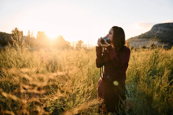 stock image a young adult walking through the meadow with her vintage camera, enjoying and photographing the sunset.