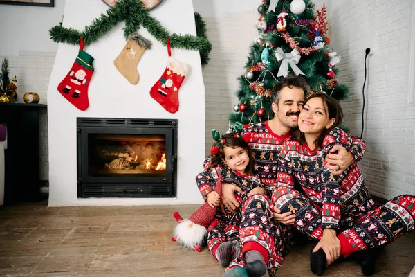 Bir aile, baba, anne ve kız, aynı Noel pijamalarını giyiyorlar, şöminenin önünde aile fotoğrafları çekiyorlar ve bir Noel ağacı. Sahne, tatil sezonunun neşesini, sevgisini ve birlikteliğini temsil ediyor.