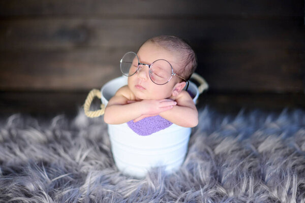 Close-up shots of a newborn baby girl, inside a white metal cube and wearing huge glasses