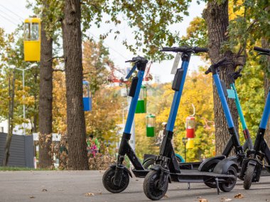 Sonbahar parkında asfalt yolda renkli kablolar olan elektrikli scooterlar. Kharkiv şehir eğlence parkında halka açık e-scooter parkı