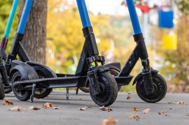 Sonbahar parkında asfalt yolda renkli kablolu elektrikli scooterlar var. Kharkiv şehir eğlence parkında halka açık e-scooter parkı