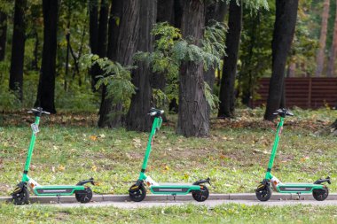 Green Electric Scooter 'lar yeşillik caddesinde park halindeler. Genel e-scooter, popüler çevre taşımacılığı