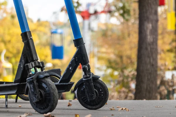 在秋季公园的柏油路上 电动滑板车的车轮与彩色模糊的电缆背景紧密相连 公共电子单车停泊在市区康乐公园内 — 图库照片