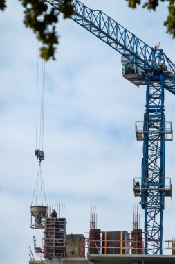 İnşaat alanında bulutlu gökyüzü ile birlikte beton dolu mavi bir vinç.