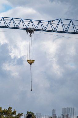 Bulutlu gökyüzü arka planında inşaat alanında büyük ağırlıkları kaldırmak için mavi uzun vinç projeksiyon kolu