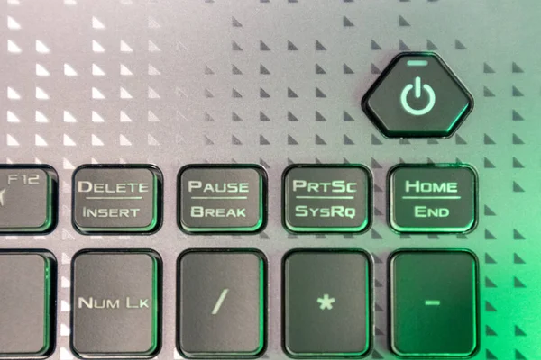 Turn on and off power button with green light. Gaming grey notebook keyboard close-up. Tech, IT, electronics, computer science background