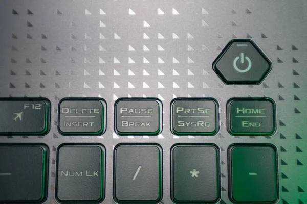 Turn on and off power key in green light. Gaming grey notebook keyboard close-up. Tech, IT, computer science background
