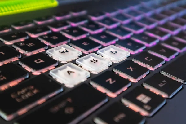 Highlighted gaming keys with pink purple gradient light and blurred background. Powerful dark notebook keyboard close-up. Tech, IT, e-sport, computer science background
