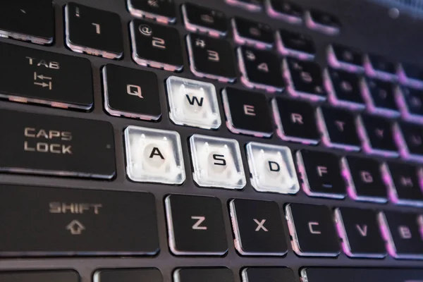 Gaming keys with pink purple gradient light and blurred background. Powerful dark notebook keyboard close-up. Tech, IT, e-sport, computer science background
