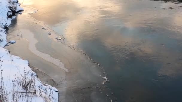 雪に覆われた冬の冷たい川の水に太陽が輝きます 日没時の水の流れ静止画 — ストック動画