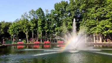 Yazın yeşil dinlenme alanındaki bir gölün üzerinde parlak gökkuşağı olan parlak, ışıl ışıl bir çeşme. Central City Park 'taki turistik ilgi merkezi, Kharkiv Ukrayna