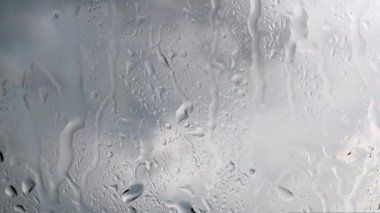 Cam pencereye yağmur yağıyor, yakın plan bulutlu gri arka plan ile su damlıyor. Huysuz yağmurlu görüntüler