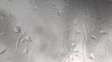 Pencereye yağmur yağıyor, cama yakın plan bulutlu gri arka plan ile su düşüyor. Huysuz yağmurlu görüntüler