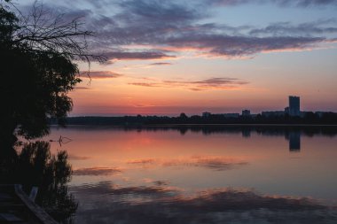 Gölde gün doğumu, bulutlu gökyüzü sakin ayna su yüzeyine yansıyor. Nehir kenarında renkli bir sabah