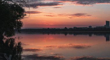 Bulutlu gökyüzü ve sakin ayna su yüzeyi ile gölde gün doğumu. Nehir kenarında renkli bir sabah