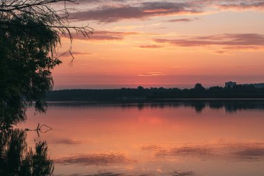 Gölde gün doğumu, bulutlu gökyüzü sakin ayna su yüzeyine yansıyor. Nehir kenarında huzurlu bir sabah
