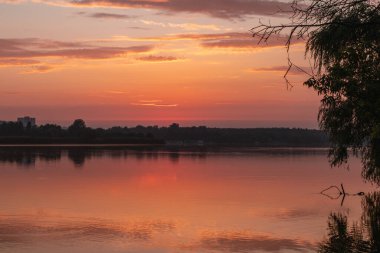 Gölde gün doğumu sakin ayna su yüzeyine yansıyan bulutlarla. Nehir kenarında renkli bir sabah
