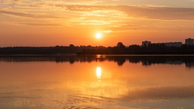 Gölde parlayan güneş ışığı sakin ayna su yüzeyine yansıyan bulutlar. Şehir parkındaki nehir kenarında renkli bir sabah