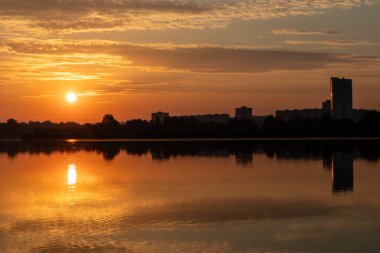 Gölde parlayan güneşin doğuşu bulutlu gökyüzünün suya yansıması. Şehir parkında huzurlu bir sabah