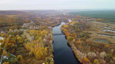 Ukrayna 'daki Korobovy Hutora' da (Koropove köyü) sonbahar ağaçları ve dinlenme alanı ile nehir boyunca uzanan köprüde havadan aşağıya doğru görüş.