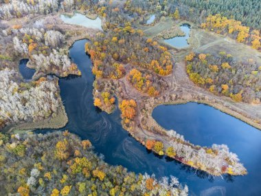 Nehir kıyısındaki renkli ağaçlarla nehir vadisine sonbahar havası bakıyor. Mavi sakin suyla sonbahar doğası