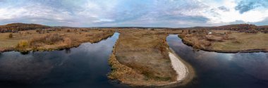 Sonbahar vadisinde nehir eğrisi üzerinde geniş hava manzarası sazlıklar, ağaçlar, toprak yol ve Ukrayna 'da destansı bulutlu gökyüzü