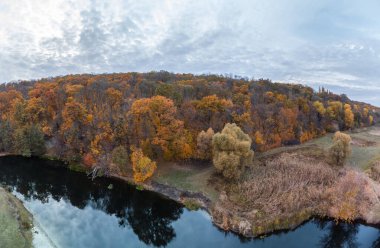 Aerial panorama of river shore near autumn forest and grey cloudy sky in Ukraine clipart