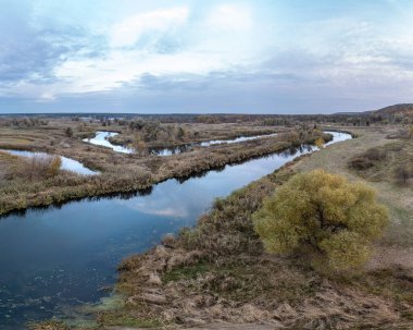 Ukrayna 'da bulutlu gökyüzü ile nehir kenarında büyüyen ağaçlarla dolu havadan nehir eğrisi manzarası