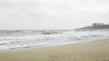 Kıyılarda fırtınalı gri bulutlu hava dalgaları Odesa şehrinde kumlu plajı vuruyor.