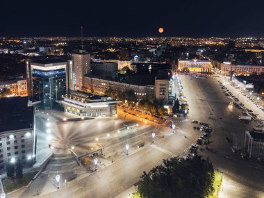 Şehir merkezindeki Kharkiv şehrinde otelin aydınlattığı Özgürlük Meydanı ve gökyüzünde büyük turuncu ay.