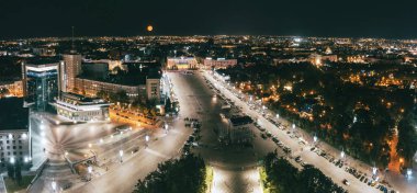 Şehir merkezindeki Harkiv şehrinde gökyüzünde aydınlık binası ve büyük turuncu ayı olan Özgürlük Meydanı.