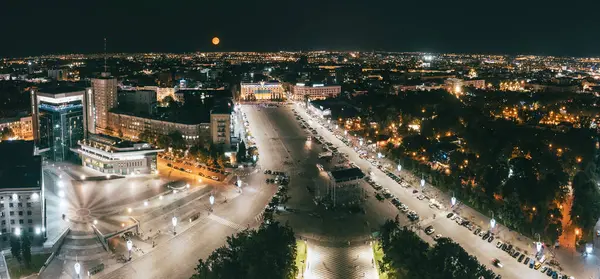 Şehir merkezindeki Harkiv şehrinde gökyüzünde aydınlık binası ve büyük turuncu ayı olan Özgürlük Meydanı.