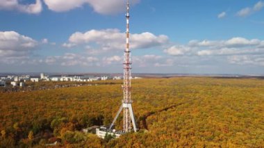 Renkli bir sonbahar ormanında, parlak yaprakları ve bulutlu mavi gökyüzü olan yüksek televizyon kulesinin gökyüzü.