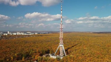 Hava aracı, altın yaprakları ve bulutlu mavi gökyüzü ile renkli sonbahar ormanlarında yüksek bir TV kulesine doğru uçar.