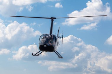 Bulutlu arka planda gezinen parlak siyah helikopter.