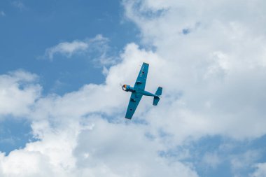 Mavi Yak-52 uçak, hava gösterisindeki manzara bulutları içinde akrobatik hareketlerle uçuyor.