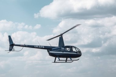 Kharkiv, Ukrayna - 29 Ağustos 2021: Mavi Helikopter Robinson R44 Raven 1 KharkivAviaFest hava gösterisinde bulutlarla havada süzülüyor