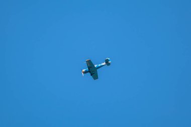 Yakovlev Yak-52 iki koltuklu eğitim uçağı hava gösterisinde açık mavi gökyüzü arka planında uçuyor.
