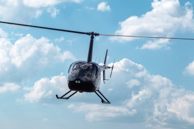 Bulutlu arka planda uçan parlak siyah bir helikopter.