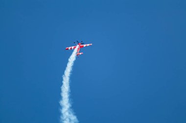 Parlak kırmızı uçak Sukhoi Su-31, hava gösterisinde mavi gökyüzünde ters dublörlük yapıyor.