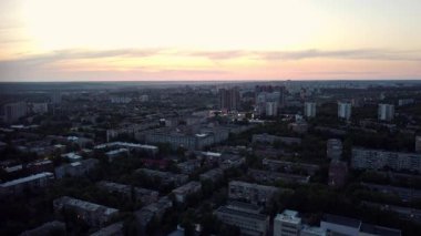 Alacakaranlıktaki Kharkiv şehrinin yerleşim bölgesinde şehir ışıkları ve günbatımı gökyüzü ile uçan hava manzarası