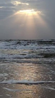 Destansı fırtınalı deniz, kumlu sahil kıyısı. Güneş ışığı kara bulutlarda parlıyor.