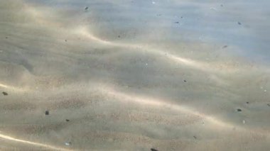 Güneş ışığı kristal gibi berrak sularda akar, deniz tabanındaki kum dalgaları üzerinde ışık desenleri oluşturur.