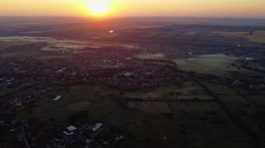Kırsal arazinin üstündeki hava gündoğumu manzarası, tarım arazisi ve sabah sisli evler.