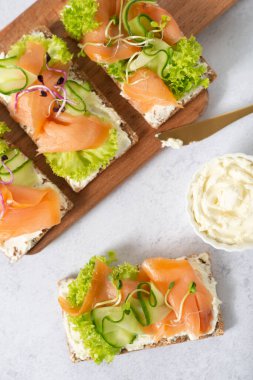 Tütsülenmiş somon, erimiş peynir ve tere salatası ile ev yapımı kızarmış ekmek. Beyaz tahta üzerinde. Mısır gevreği ekmeğinde somonlu tost..