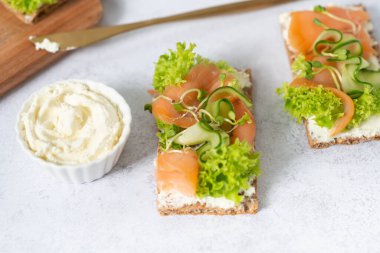 Tütsülenmiş somon, erimiş peynir ve tere salatası ile ev yapımı kızarmış ekmek. Beyaz tahta üzerinde. Mısır gevreği ekmeğinde somonlu tost..