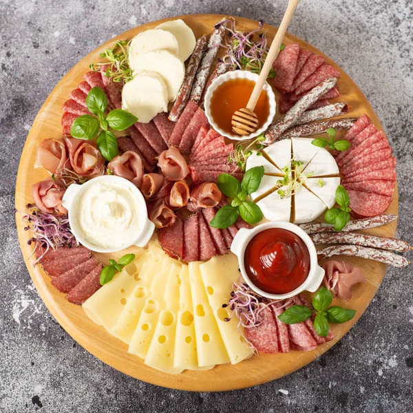 stock image Wooden plate with delicacies. Brie cheese, blue cheese, salami, prosciutto on a wooden board.