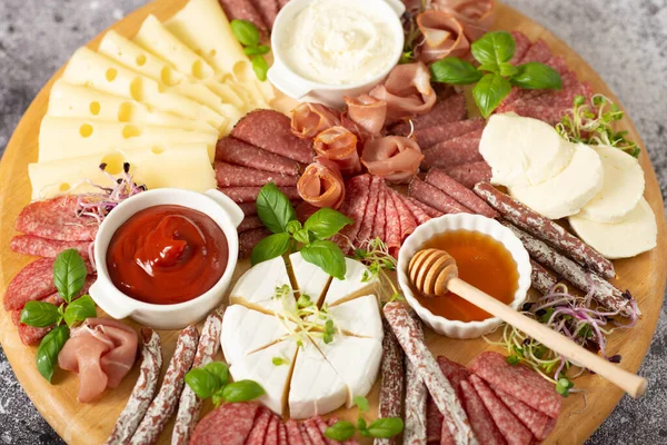 stock image Delicacies. Cheese, prosciutto, salami on a wooden square board on a concrete background.